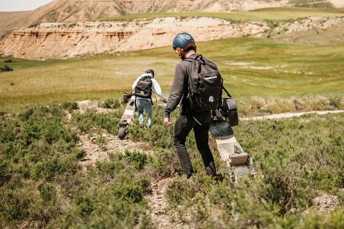 Two riders carrying their Stern' boards across heathland, wearing the backpack battery